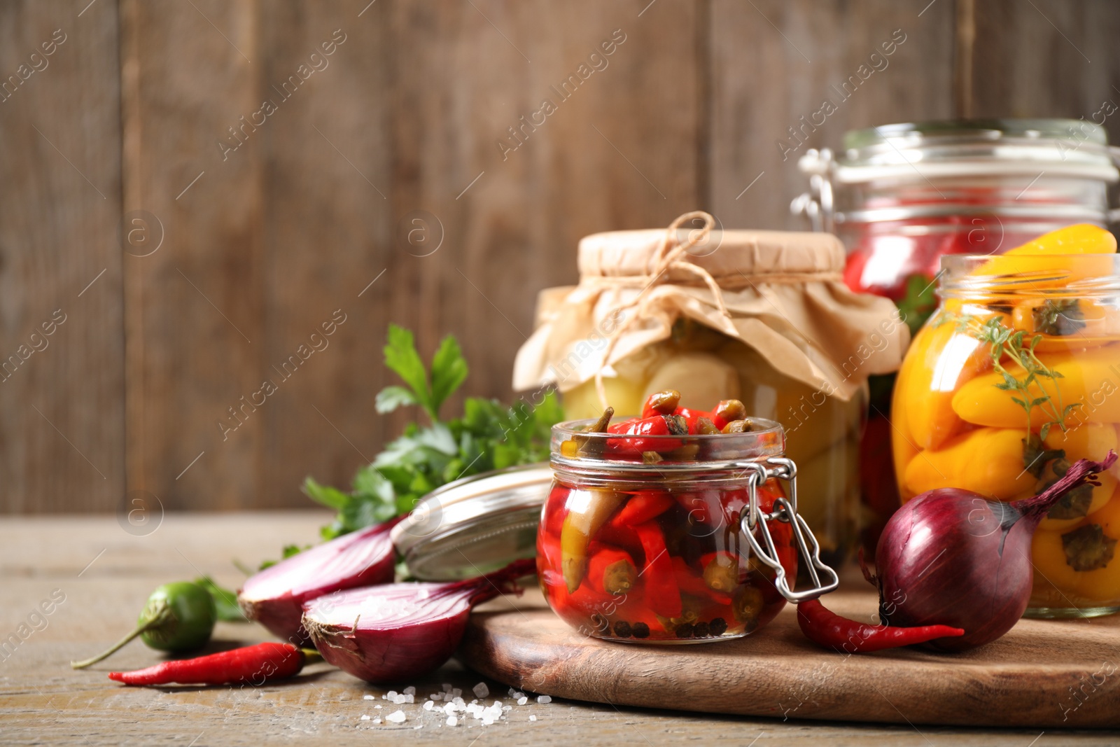 Photo of Glass jars with pickled peppers on wooden table. Space for text