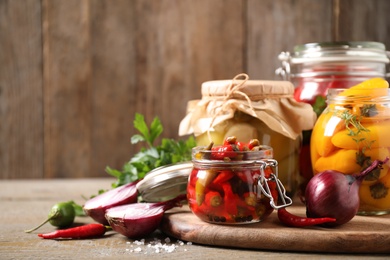 Glass jars with pickled peppers on wooden table. Space for text