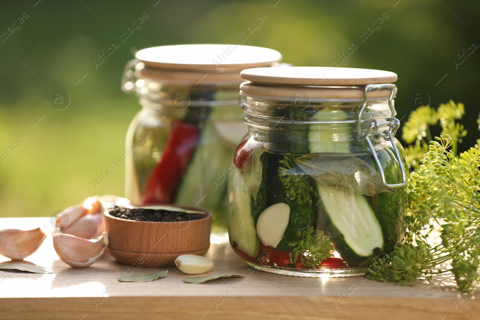 Photo of Jars of delicious pickled cucumbers and ingredients on wooden table against blurred background, closeup
