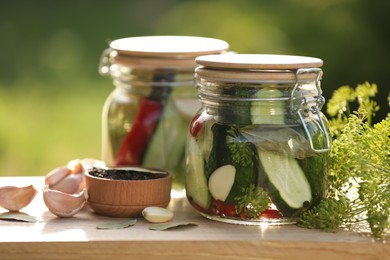Photo of Jars of delicious pickled cucumbers and ingredients on wooden table against blurred background, closeup