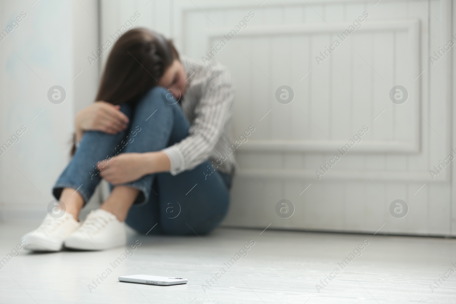 Photo of Lonely woman sitting on floor and smartphone on foreground, space for text