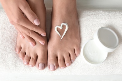 Photo of Woman applying foot cream on white towel, top view. Spa treatment