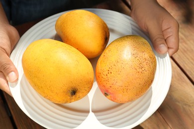Woman holding plate with tasty mangoes at wooden table, closeup