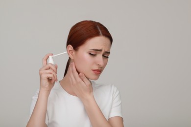Photo of Unhappy woman using ear spray on light grey background. Space for text