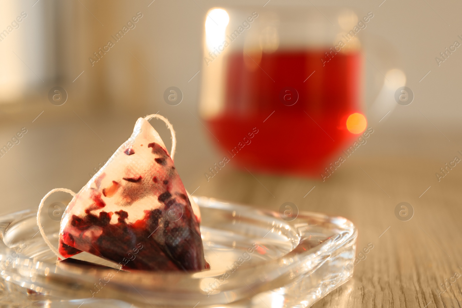 Photo of Glass saucer with used tea bag on wooden table, closeup