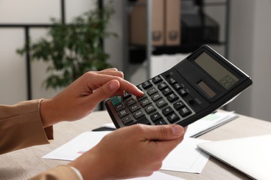 Photo of Woman using calculator at table in office, closeup
