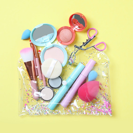 Plastic cosmetic bag with makeup products and beauty accessories on yellow background, flat lay