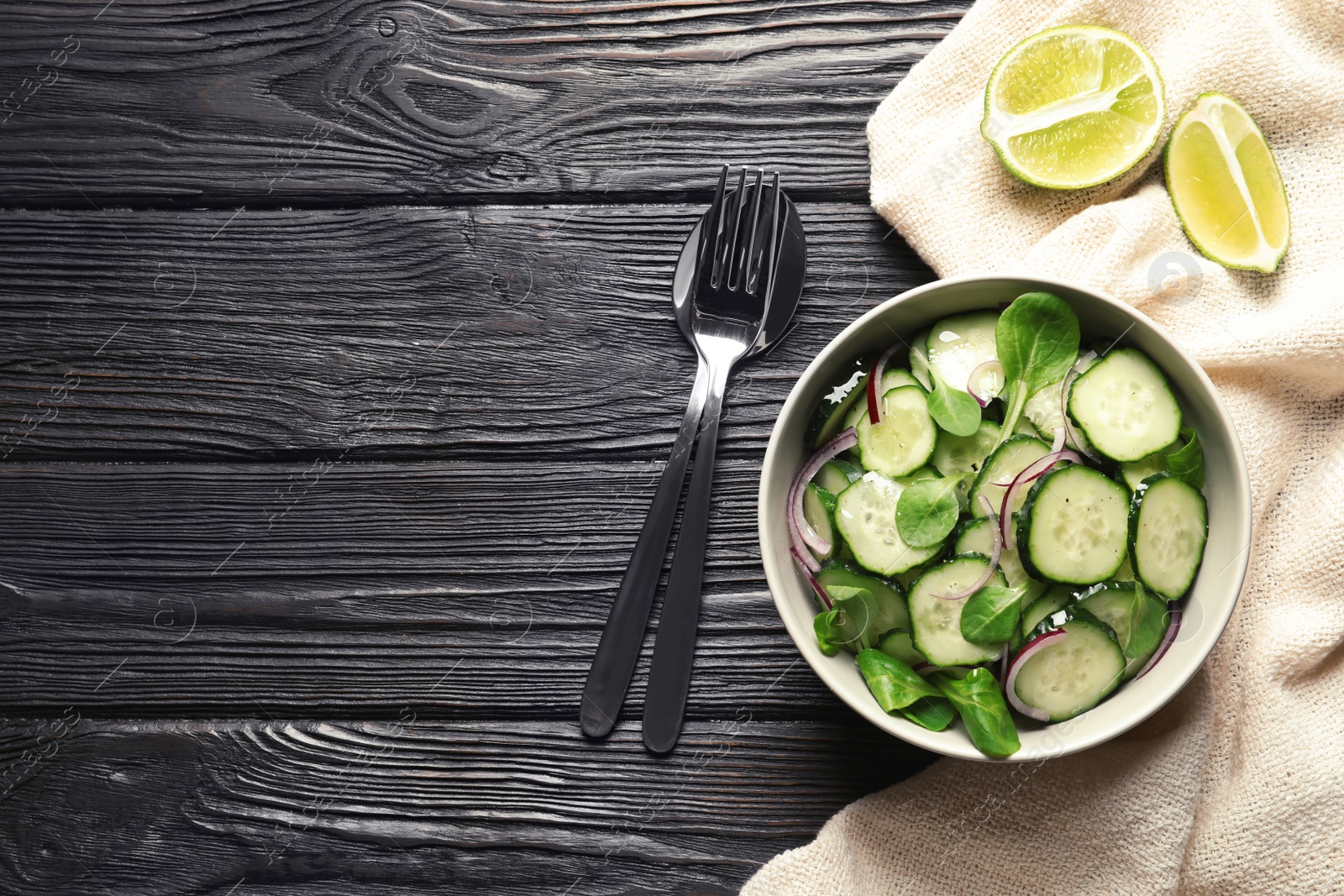 Photo of Delicious cucumber salad with onion and spinach in bowl served on wooden table, top view. Space for text