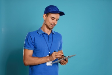 Happy young courier with tablet on blue background. Space for text