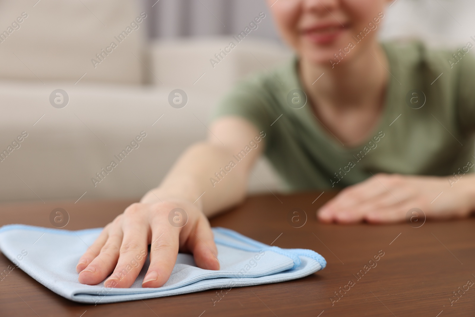 Photo of Woman with microfiber cloth cleaning wooden table in room, closeup