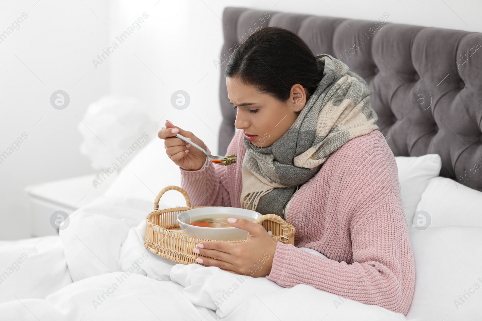 Photo of Sick young woman eating soup to cure flu in bed at home