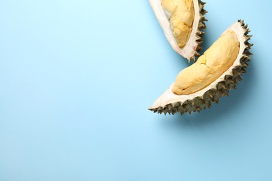 Photo of Pieces of fresh ripe durian on light blue background, flat lay. Space for text