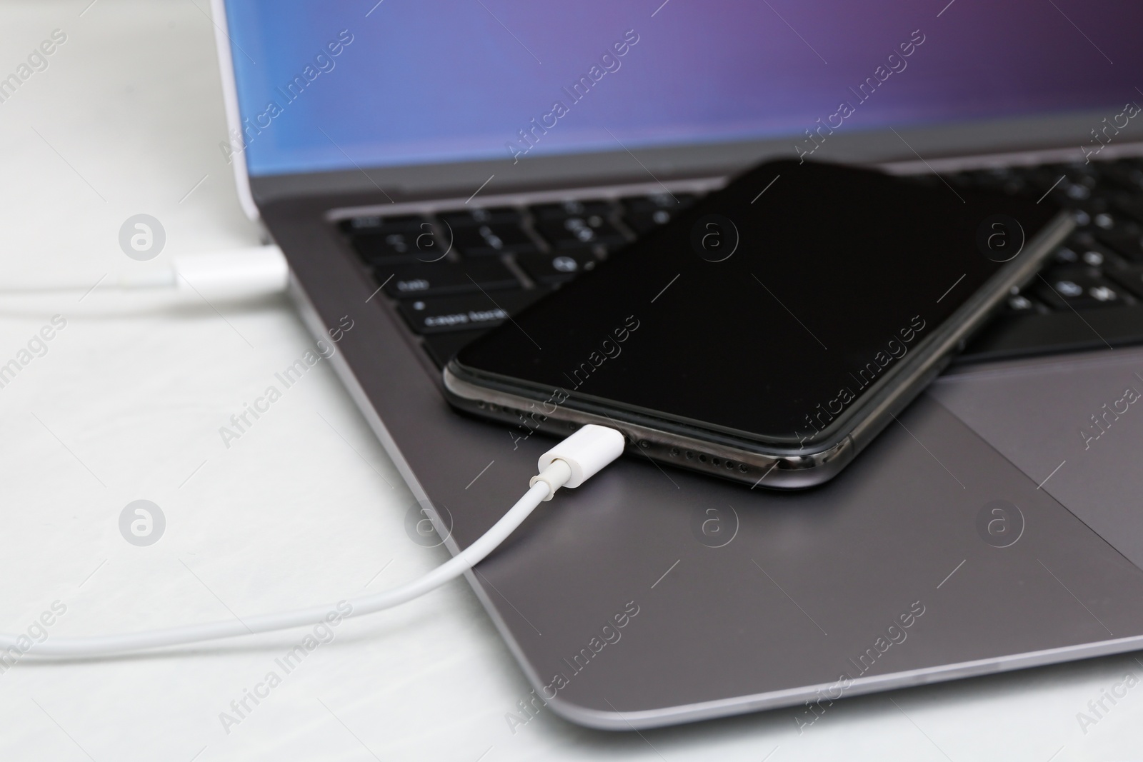 Photo of Smartphone connected with charge cable to laptop on light table, closeup