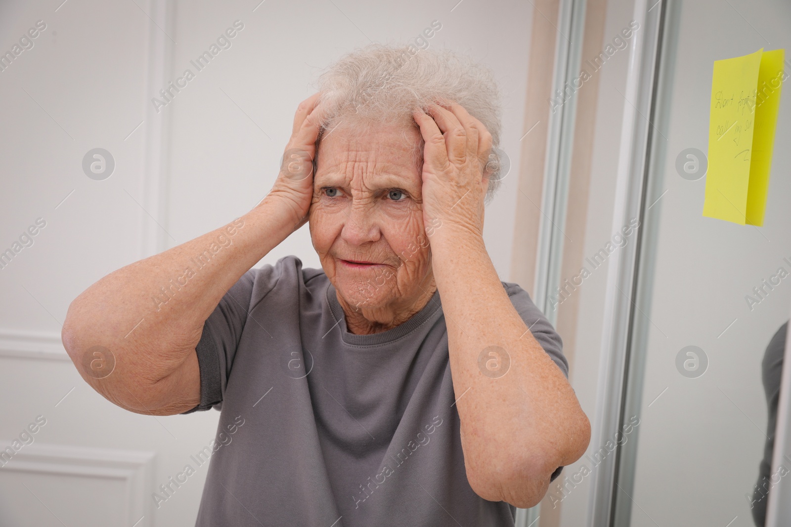 Photo of Forgetful senior woman near mirror with reminder note indoors. Age-related memory impairment