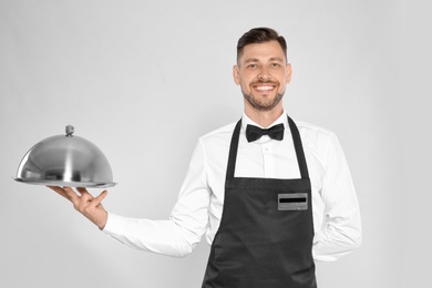 Photo of Handsome waiter holding metal tray with lid on light background