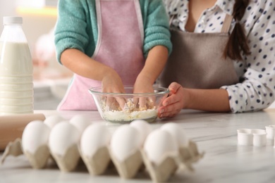 Photo of Mother and daughter making dough at table in kitchen, closeup