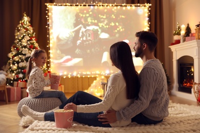 Photo of Family watching movie on projection screen in room decorated for Christmas. Home TV equipment