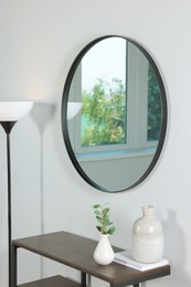 Stylish round mirror on white wall over table in room