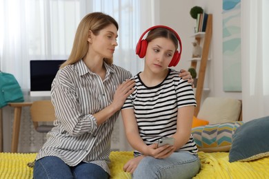 Photo of Mother comforting her upset teen daughter with headphones at home