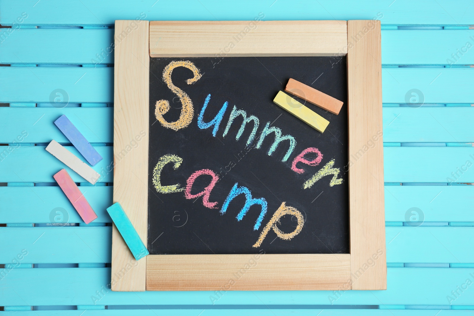 Photo of Words SUMMER CAMP written with colorful chalk on small blackboard, top view