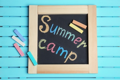 Words SUMMER CAMP written with colorful chalk on small blackboard, top view