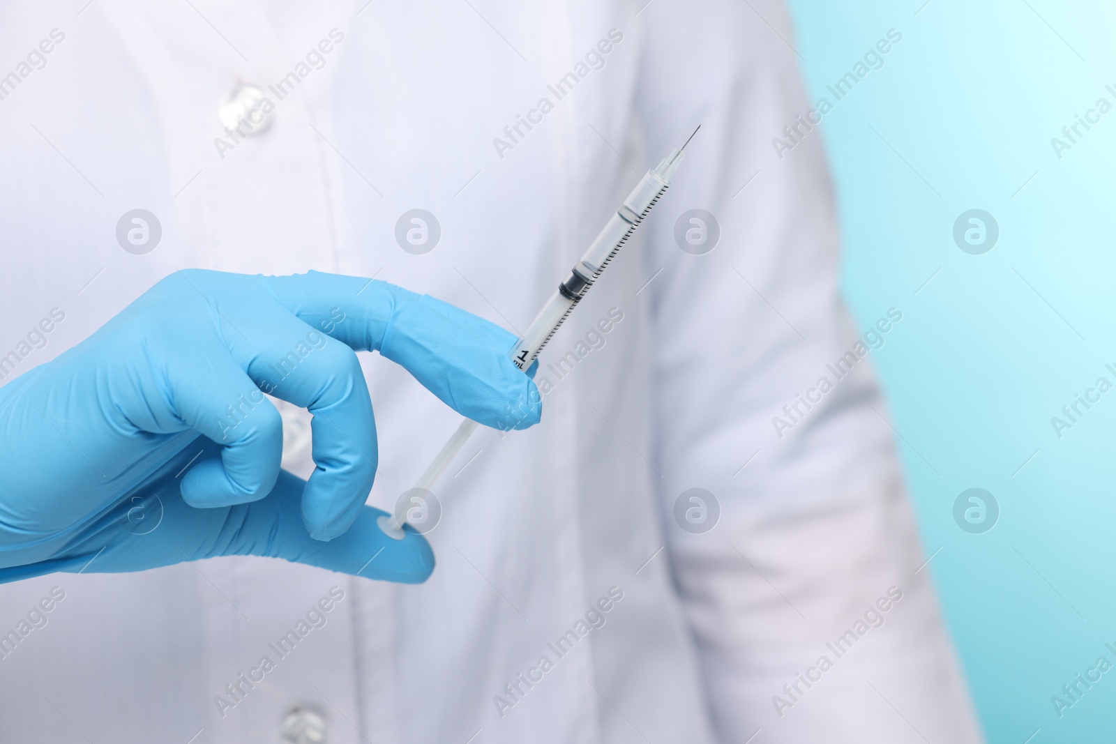 Photo of Doctor holding syringe on light blue background, closeup