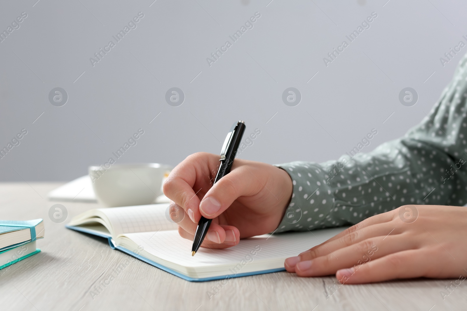 Photo of Woman writing in notebook at wooden table in office, closeup