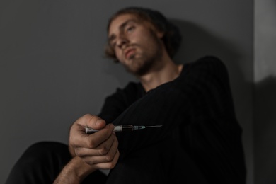 Photo of Young drug addict with syringe sitting near grey wall