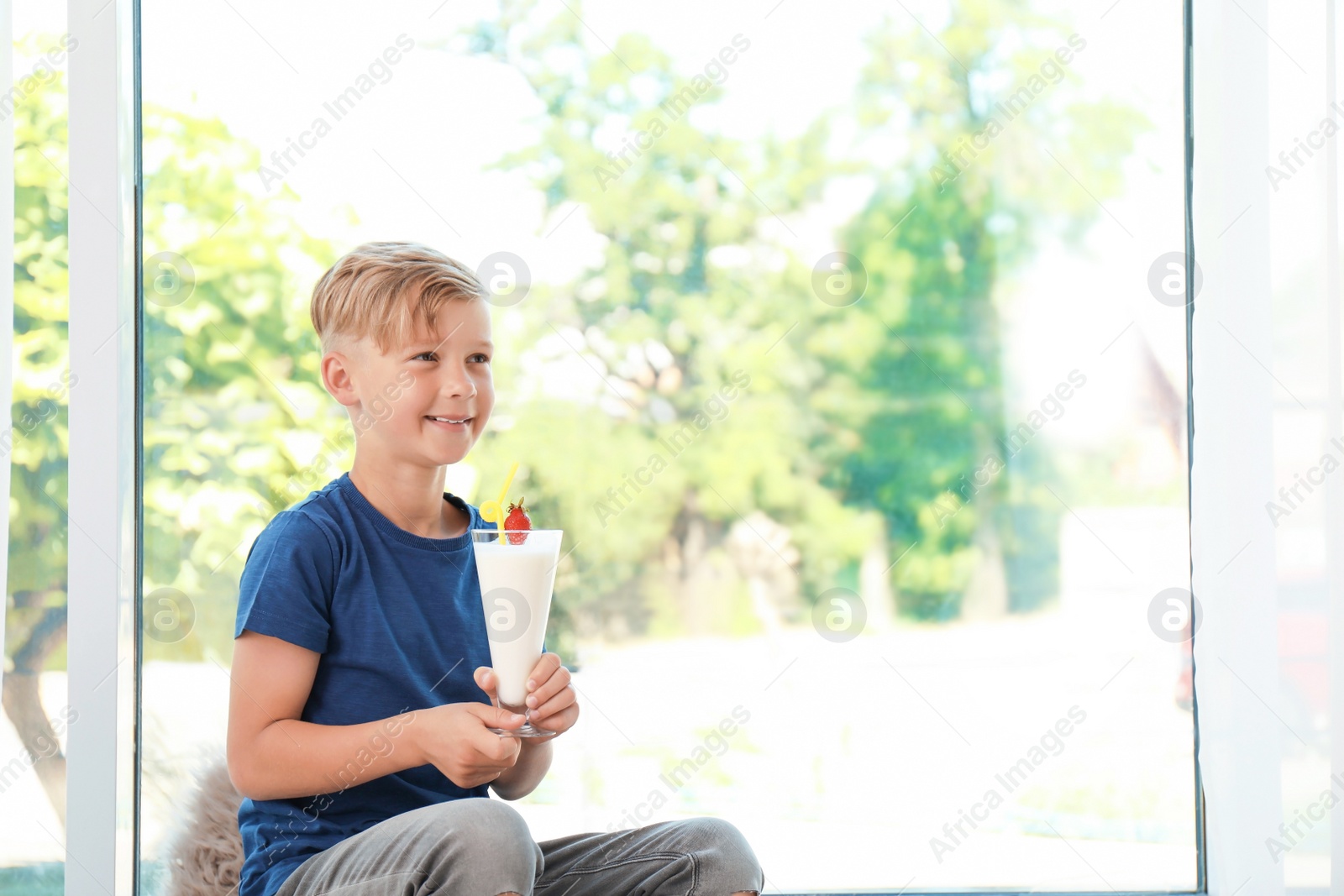 Photo of Little boy with glass of milk shake near window indoors