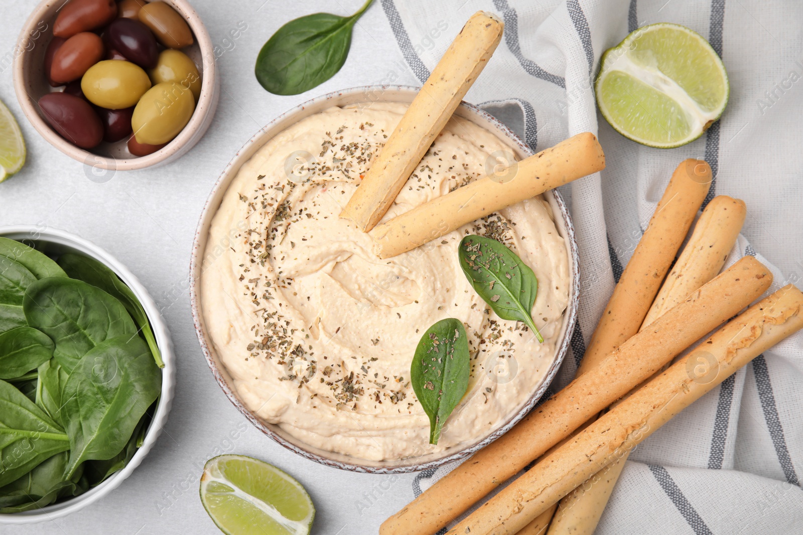 Photo of Delicious hummus with grissini sticks served on light grey table, flat lay