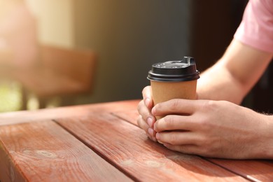 Photo of Man with takeaway coffee cup at wooden table outdoors, closeup. Space for text