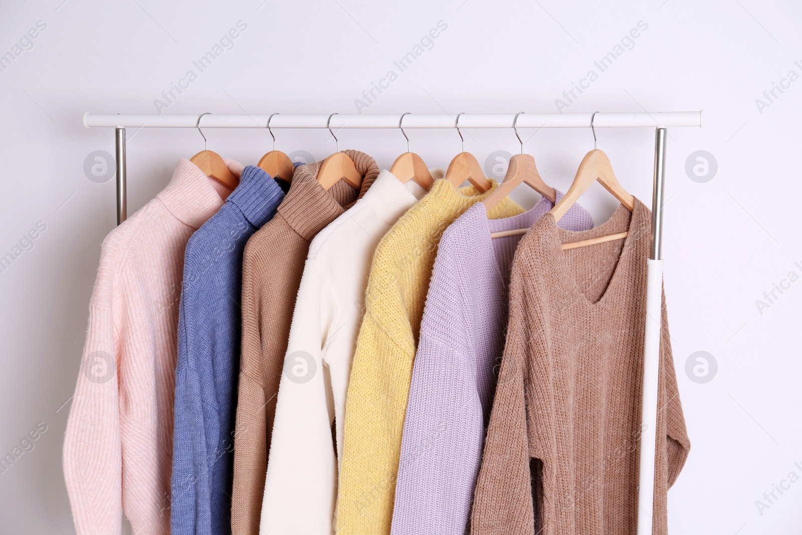 Photo of Warm sweaters hanging on rack against white background