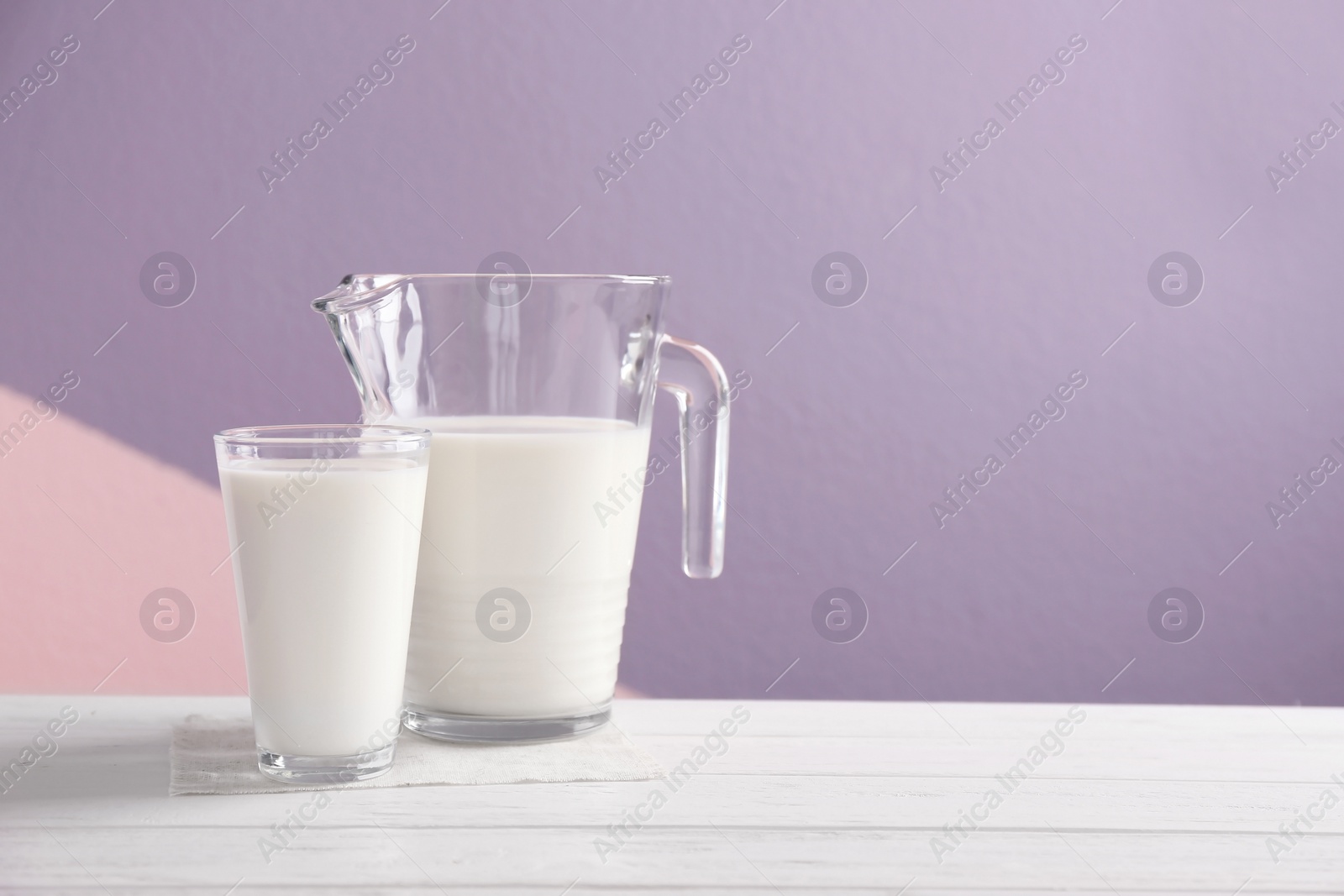 Photo of Jug and glass with milk on table against color background