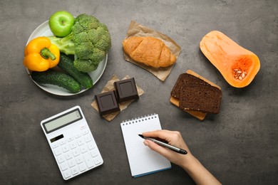 Photo of Woman calculating calories at dark grey table with food products, top view. Weight loss concept