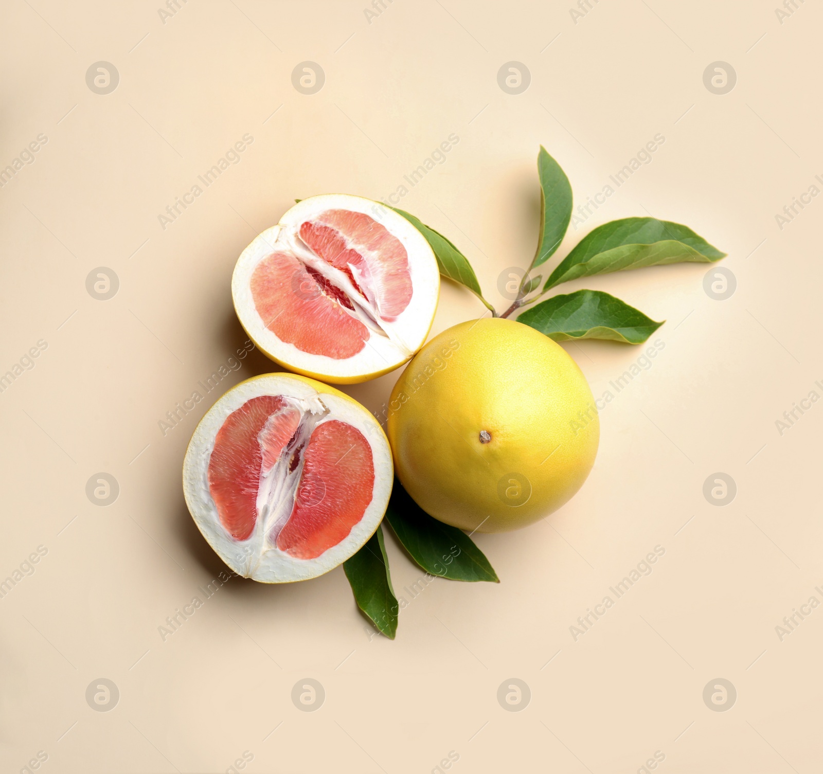 Photo of Fresh cut and whole pomelo fruits with leaves on beige background, flat lay