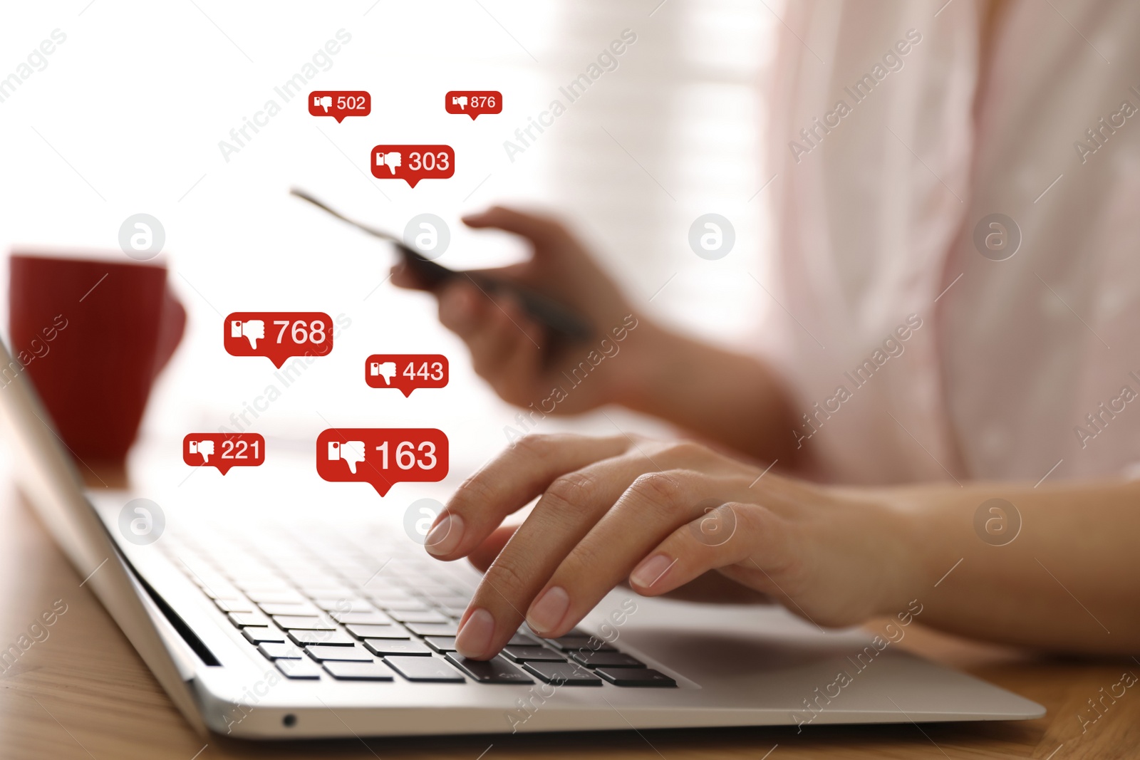 Image of Closeup view of young woman using modern laptop with smartphone indoors and virtual dislike icons at table. Cyberbullying concept