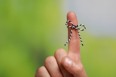 Man showing index finger with tied bow as reminder on green blurred background, closeup