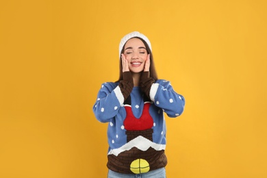 Young woman in Christmas sweater and hat on yellow background