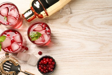 Tasty cranberry cocktail with ice cubes in glasses and bartender's tools on wooden table, flat lay. Space for text