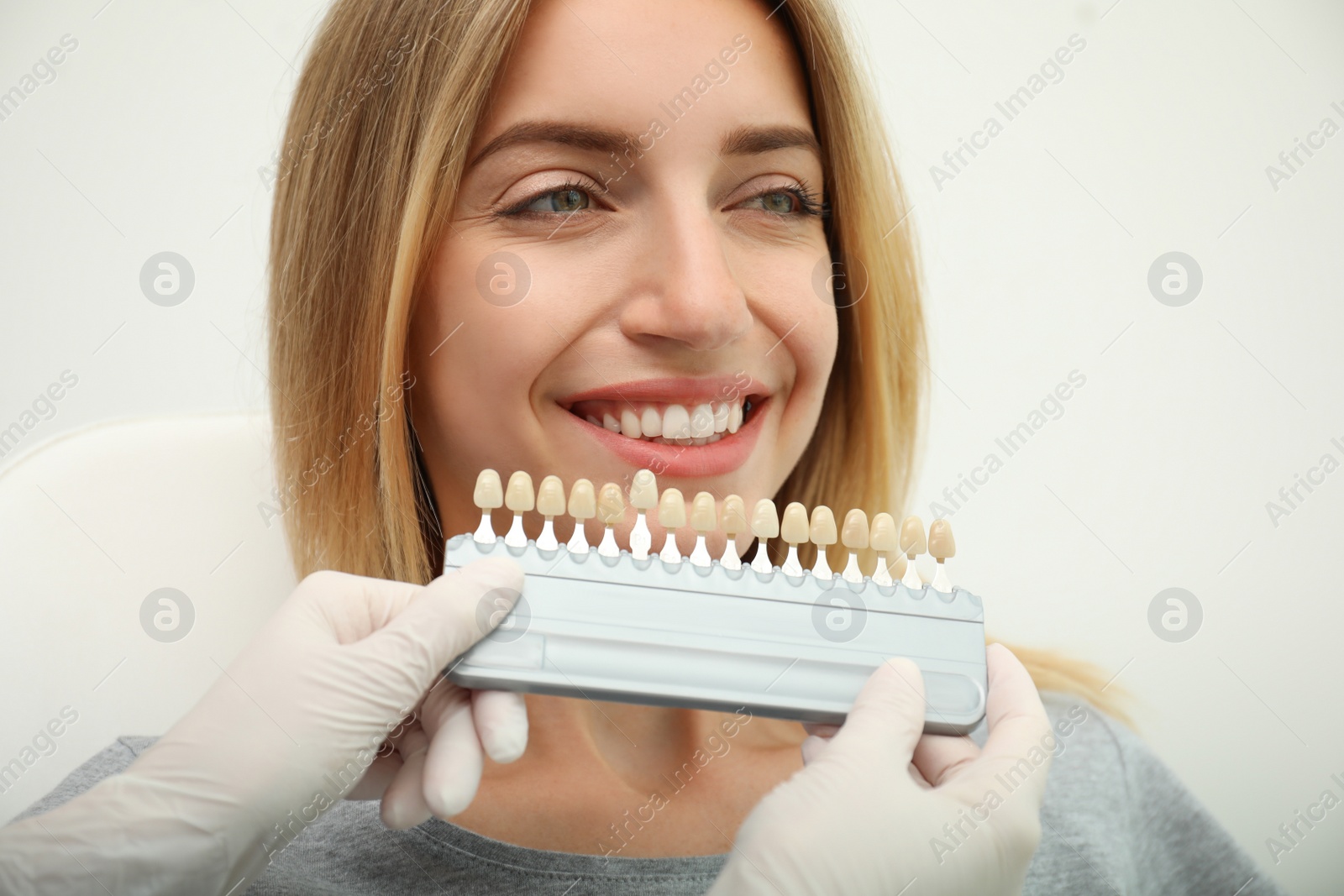Photo of Doctor matching patient's teeth color with palette on light background, closeup. Cosmetic dentistry