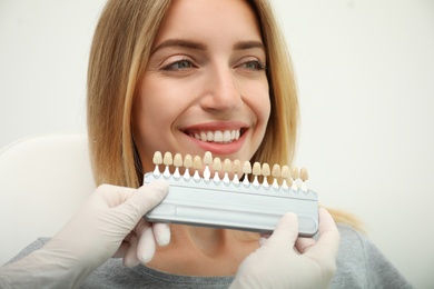 Photo of Doctor matching patient's teeth color with palette on light background, closeup. Cosmetic dentistry