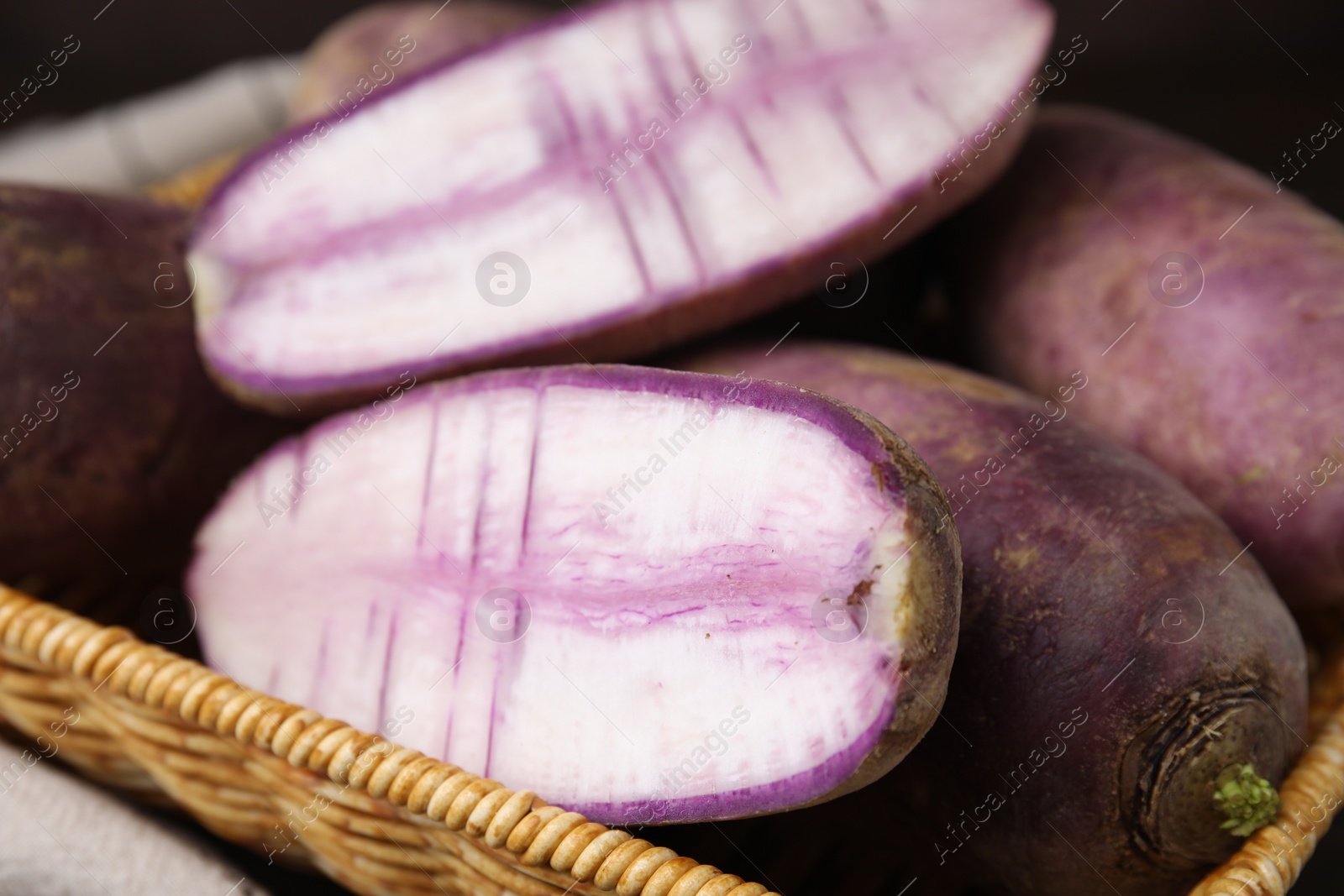 Photo of Purple daikon radishes in wicker basket on table, closeup