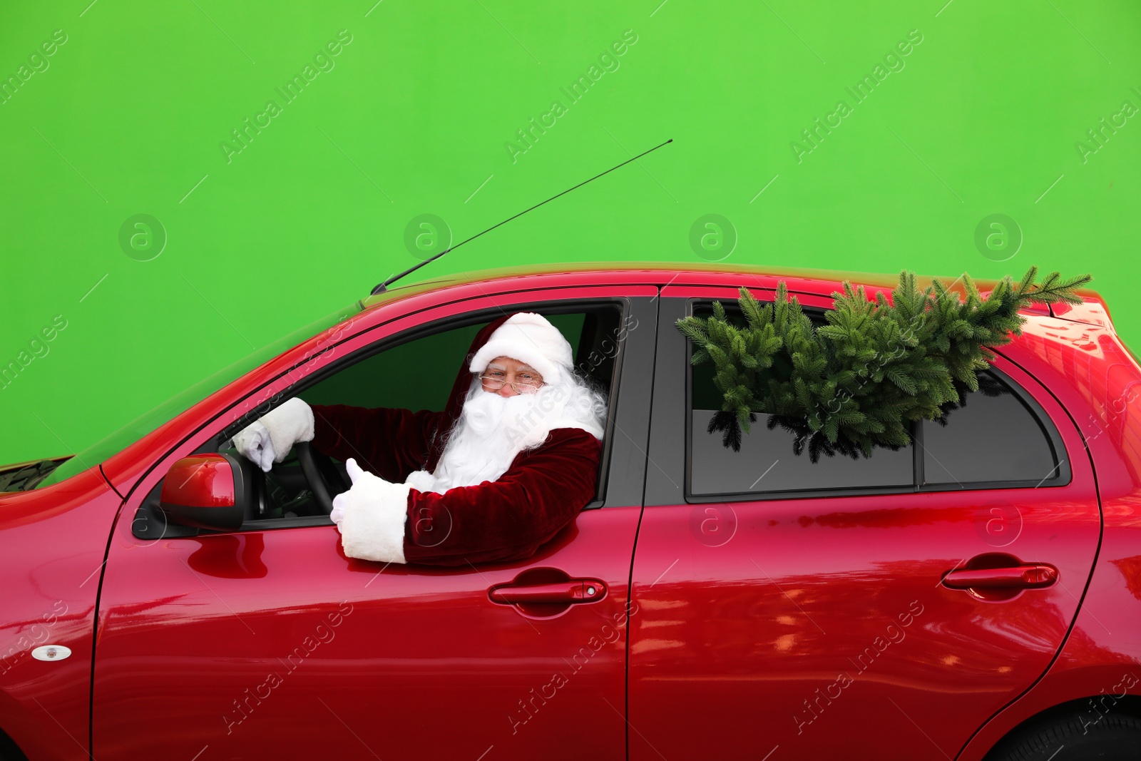 Photo of Authentic Santa Claus with fir tree driving car against green background