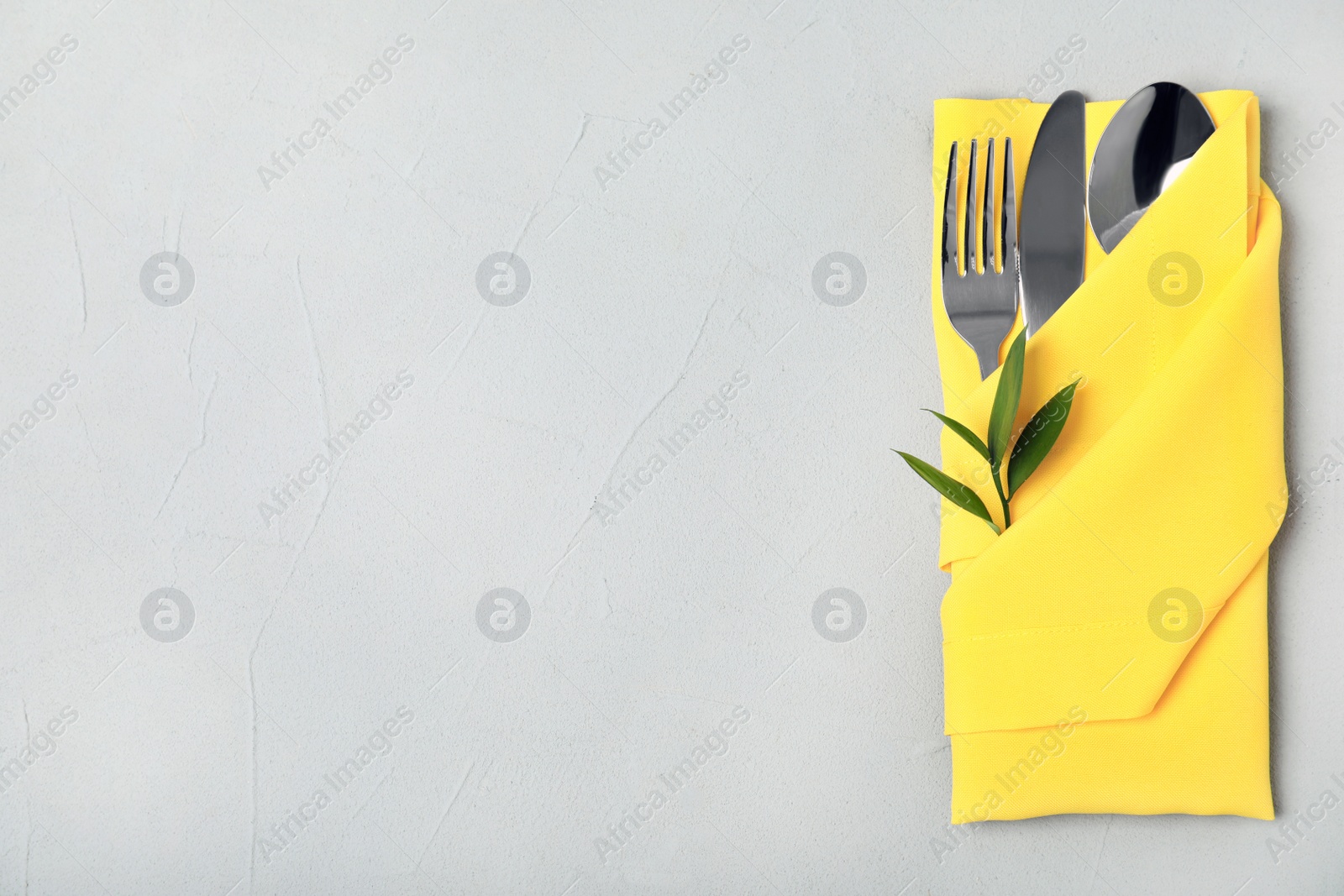 Photo of Folded napkin with fork, spoon and knife on grey background, top view. Space for text