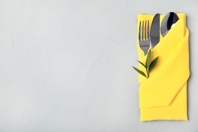 Photo of Folded napkin with fork, spoon and knife on grey background, top view. Space for text