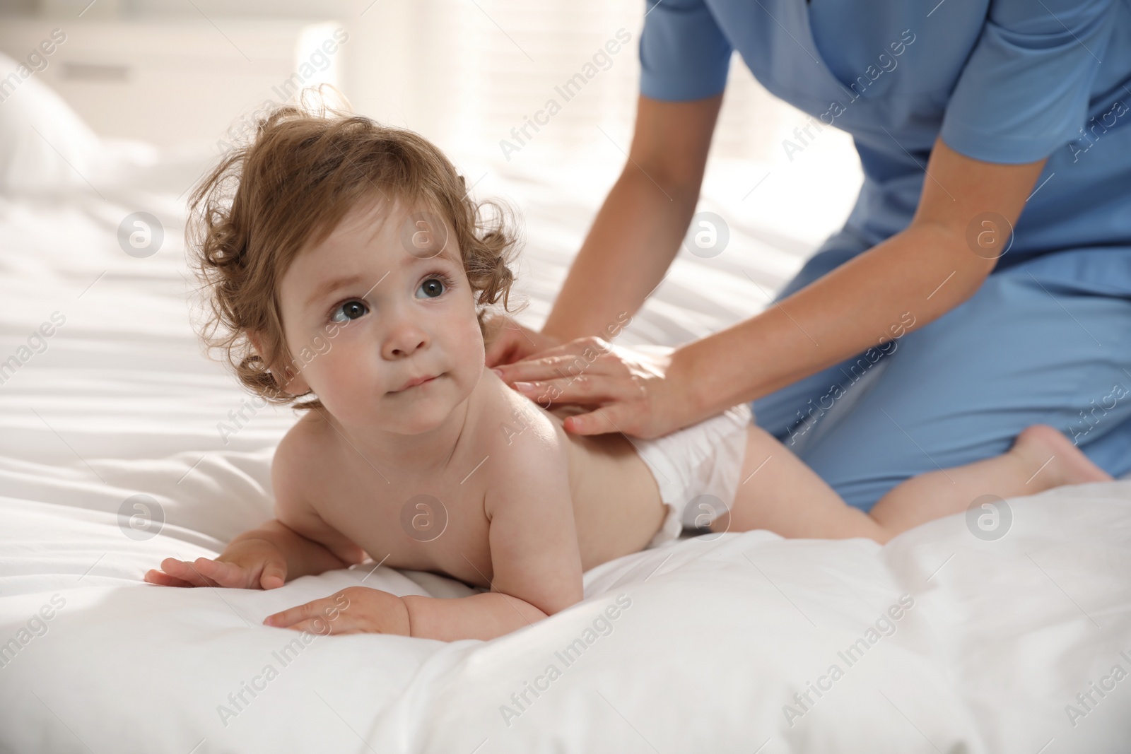 Photo of Orthopedist examining cute little baby on bed