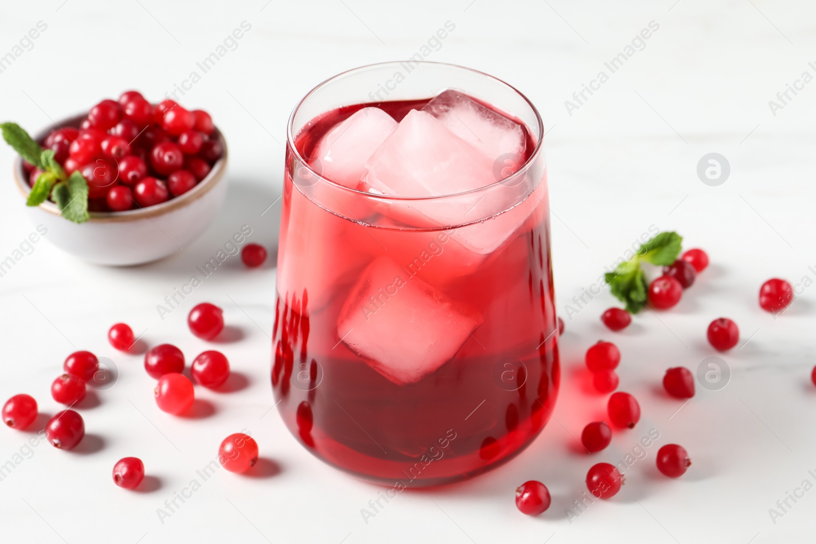 Photo of Tasty cranberry juice with ice cubes in glass and fresh berries on white wooden table, closeup