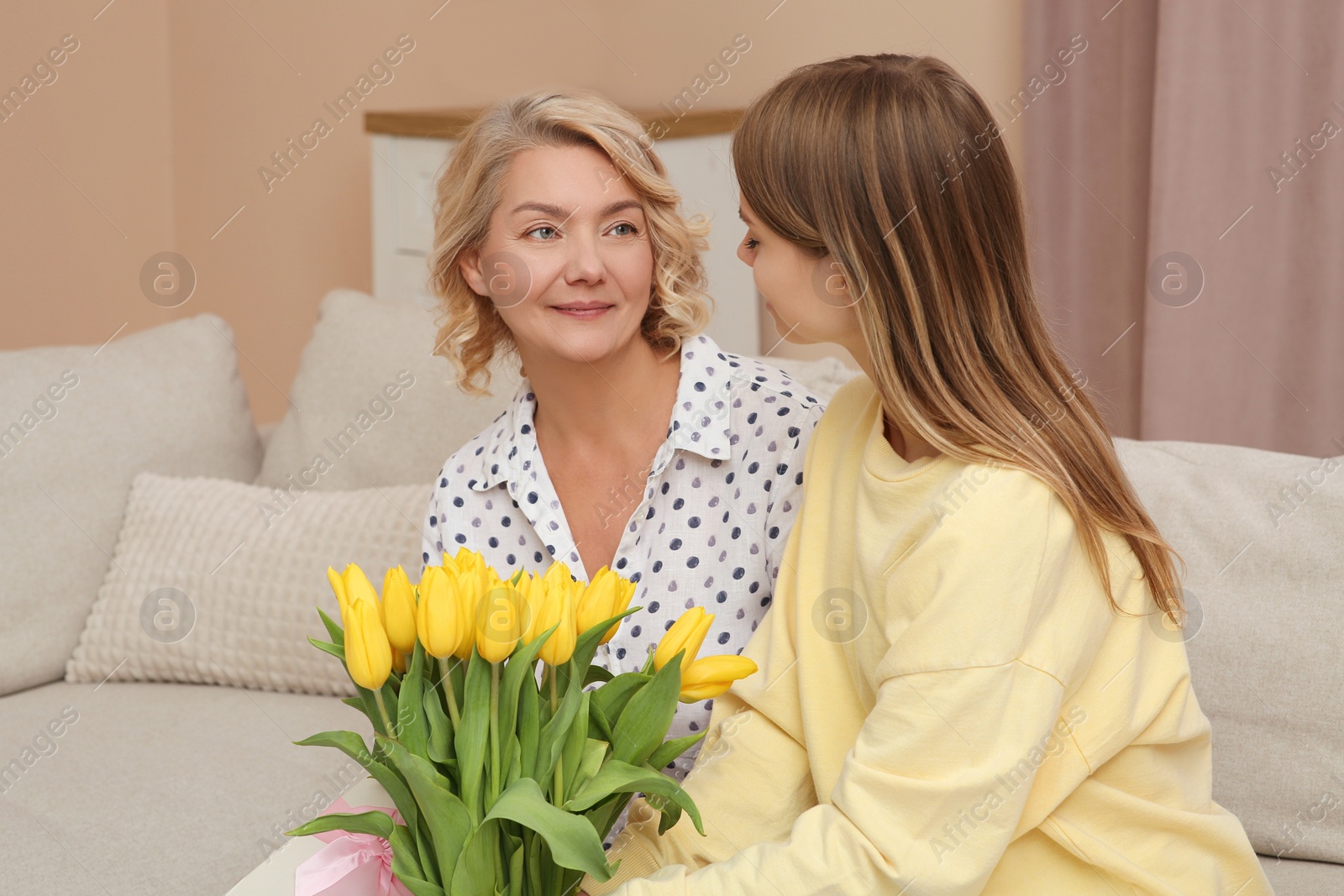 Photo of Young daughter congratulating her mom with flowers at home. Happy Mother's Day