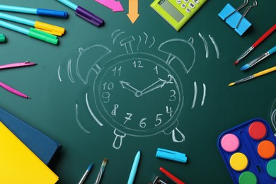 Photo of Flat lay composition with different stationery and drawn alarm clock on green chalkboard. School time
