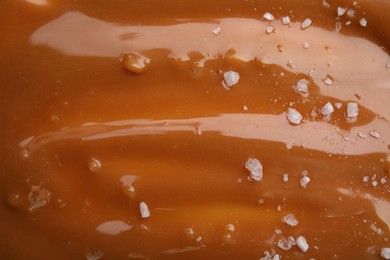 Delicious caramel sauce with sea salt as background, closeup